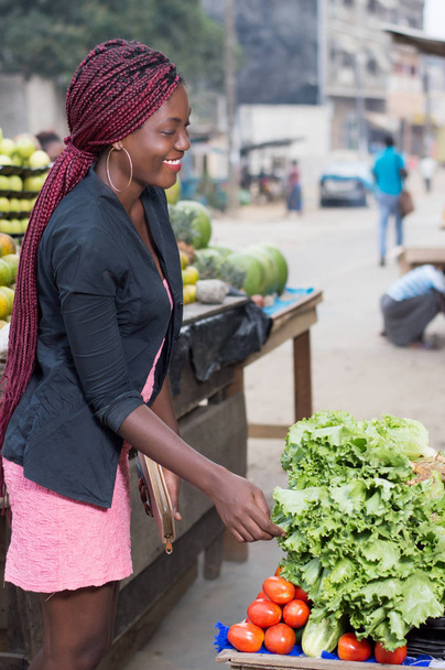 χαμογελώντας νεαρή γυναίκα ζητάει η τιμή κιλού των λαχανικών. - Φωτογραφία, εικόνα