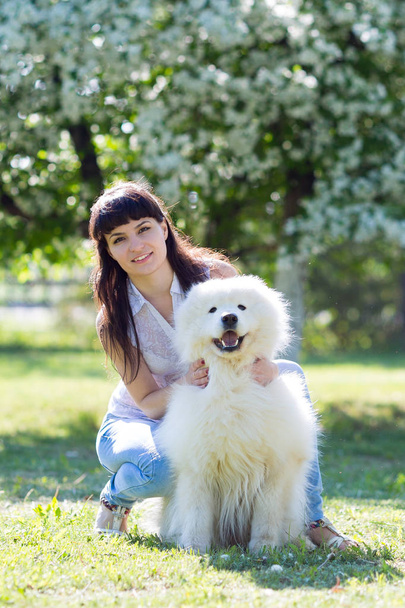 The brunette girl with a big white dog. Beautiful young girl is walking with her dog in a summer park. - Photo, Image