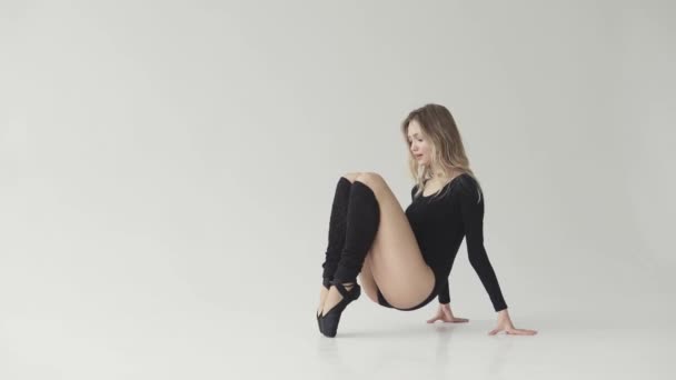 una ballerina in corpo nero e punti fa un tratto seduta sul pavimento in uno studio bianco
. - Filmati, video