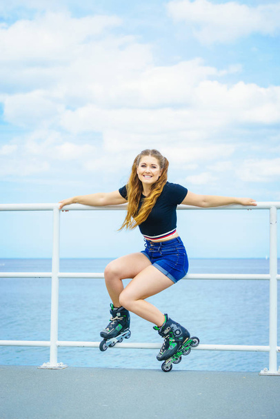 Attractive young woman wearing roller skates relaxing after ride. Fit female having fun during summer time on sea coast. - Foto, Imagem