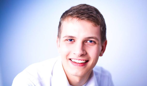 Portrait of young man smiling sitting on gray background - Zdjęcie, obraz