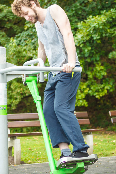 Active young man exercising on ski trainer machine. Muscular sporty guy in training suit working out at outdoor gym. Sport fitness and healthy lifestyle concept. - Valokuva, kuva