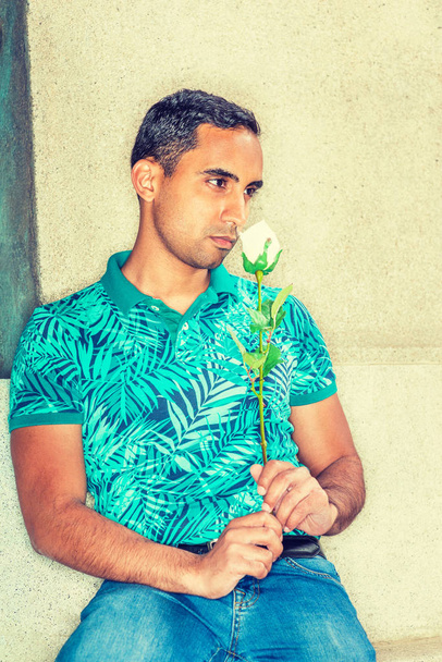 Hispán-amerikai fiatalember hiányzik, akkor gondol rólad, visel zöld mintás póló, tartja Fehér Rózsa, ül elleni wall street, New York, illatos virág, orr, szomorú - Fotó, kép