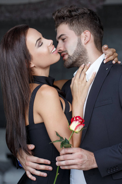 Happy νεαρό ζευγάρι με τριαντάφυλλο στην αγάπη αγκαλιά ένας τον άλλον, σε εσωτερικούς χώρους - Φωτογραφία, εικόνα
