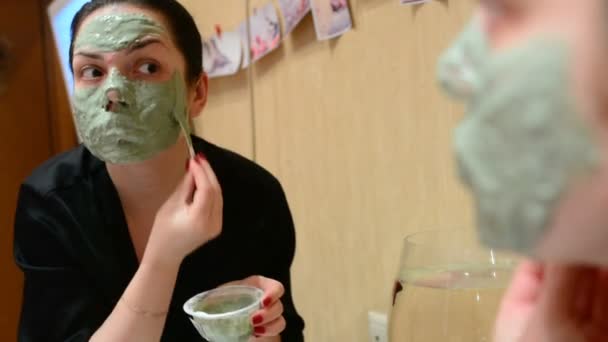 Mladá dívka použití kosmetická maska modrého jílu v místnosti před zrcadlem - Záběry, video