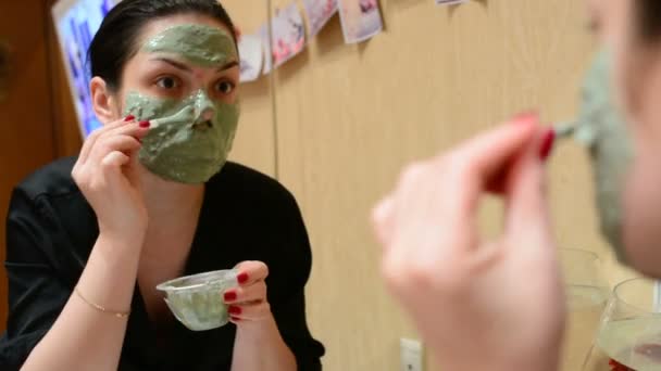 Молодая девушка надевает косметическую маску из голубой глины в комнате перед зеркалом
 - Кадры, видео