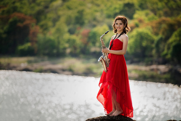Woman playing saxophone sax at sunset,Saxophonist woman in red dress - Photo, Image