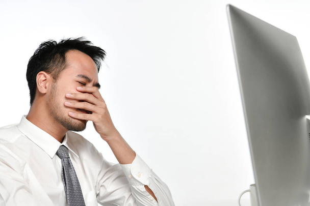 Наголошений бізнесмен прикриває обличчя рукою, працюючи на комп'ютері в офісі
 - Фото, зображення
