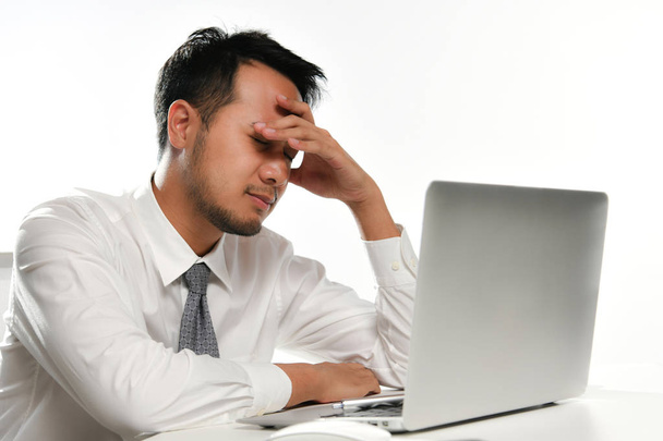 gestresster Geschäftsmann, der sein Gesicht mit der Hand bedeckt, während er im Büro am Computer arbeitet - Foto, Bild