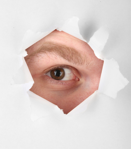 Man eye looking through hole in sheet of paper - Фото, изображение