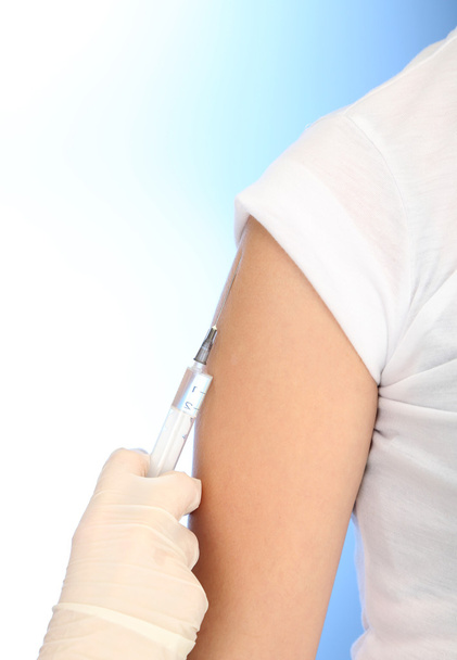 Doctor holding syringe with a vaccine in the patient shoulder, on blue background - Fotó, kép