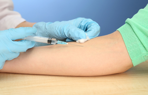 Doctor holding syringe with a vaccine in the patient hand, on blue background - Fotografie, Obrázek