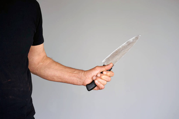 Mano de un hombre sosteniendo un cuchillo aislado sobre un fondo gris. Cuchillo de cocina grande en mano de hombre
. - Foto, imagen