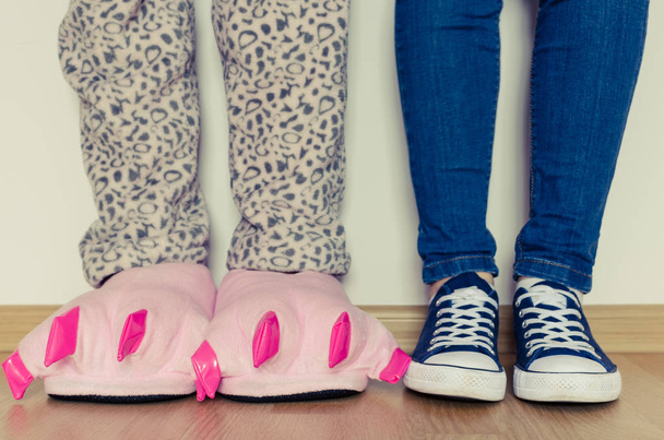 Γυναικεία πόδια σε pajama και χαριτωμένο ροζ τέρας πόδι παντόφλες με μεγάλα νύχια και ένα άλλο κλασικό τζιν και sneakers μπλε. Πρωτότυπη ιδέα, η. - Φωτογραφία, εικόνα