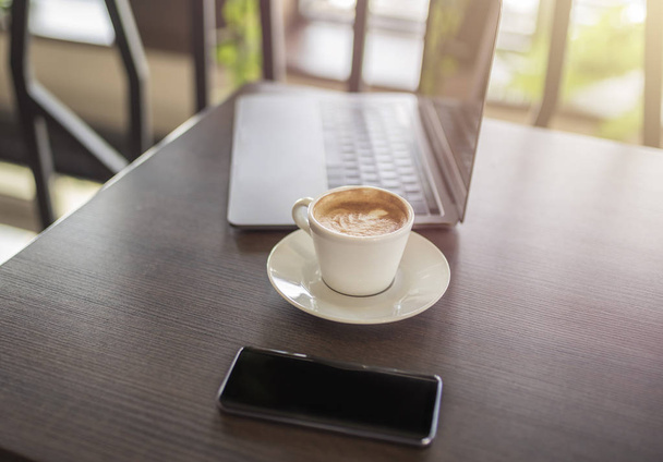 Kávé, a smartphone és a laptop a fából készült asztal. Kávé szünet. Pihenjen az idő étteremben. Süt a nap. - Fotó, kép