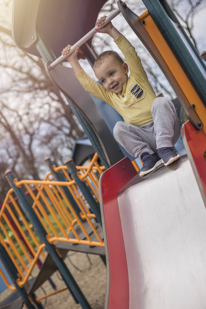 Adorable little boy having fun on playground. Active sport leisure for kids outdoor. Little boy with blue eyes in yellow shirt having fun on playground. - Фото, зображення