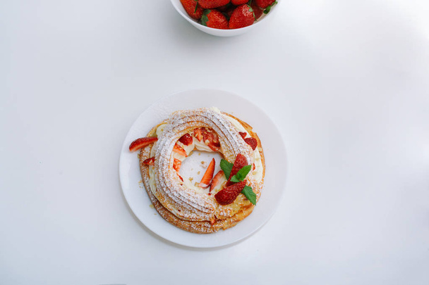Leivonnaiset kakut Pariisi Brest mansikoita, manteli, creme, sokeri jauhe ja minttu, tarjoillaan pyöreät lautaset ja lautasellinen mansikoita valkoinen pöytä ravintolassa tai kahvilassa. Huippunäkymä. Tekstipaikka
 - Valokuva, kuva