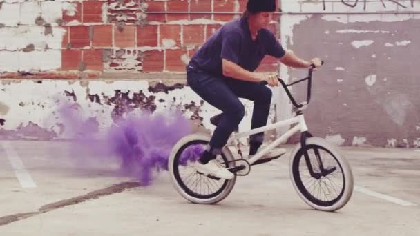 Байкер-экстремал BMX с замедленным движением делает прыжок с трюком дымовой гранаты фиолетового цвета в городской среде
 - Кадры, видео