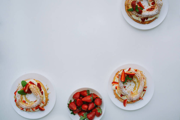 Gebäck Kuchen paris Brust mit Erdbeeren, Mandeln, Creme, Zuckerpulver und Minze, serviert auf runden Tellern und Teller mit Erdbeeren auf weißem Tisch im Restaurant oder Café. Ansicht von oben. Platz für Text - Foto, Bild