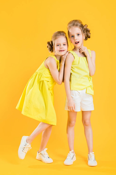 Девочки близнецов стоят вместе на желтом фоне
. - Фото, изображение