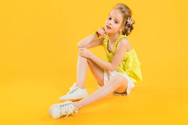A teenage girl is sitting on a yellow background. - Фото, зображення