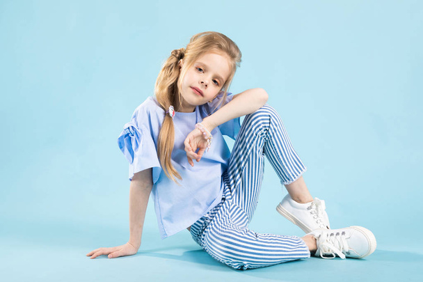 A girl in blue clothes is sitting on a blue background. - Photo, Image