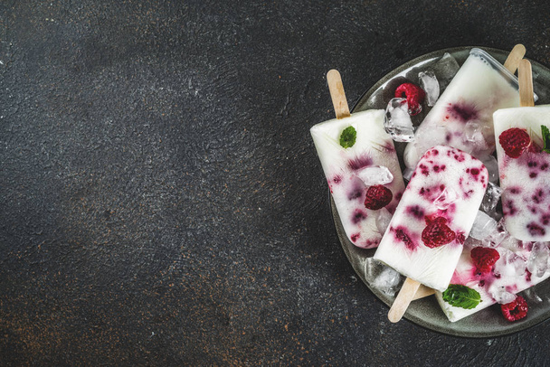 Dolci dolci estivi, gelati biologici fatti in casa ghiaccioli da lampone e yogurt, sfondo arrugginito scuro copia spazio vista dall'alto
 - Foto, immagini
