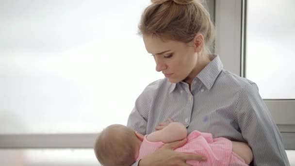 Madre cansada sosteniendo al bebé en las manos cerca de la ventana. Mujer cansada sosteniendo niño - Imágenes, Vídeo