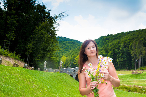 Αρκετά ευχαριστημένος Καυκάσιος κορίτσι στο ηλιόλουστο πάρκο χαμογελώντας, γελώντας, όμορφη γυναίκα με λουλούδια περίπατος στο πάρκο - Φωτογραφία, εικόνα