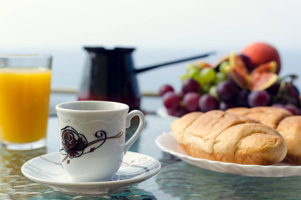 gesundes Frühstück mit einer Tasse Kaffee und einem Teller mit zartem und üppigem Croissant im Vordergrund, türkischer Kaffeekanne, einem Glas Orangensaft, einem Teller Trauben auf dem Tisch im Hintergrund. Kopierraum. - Foto, Bild