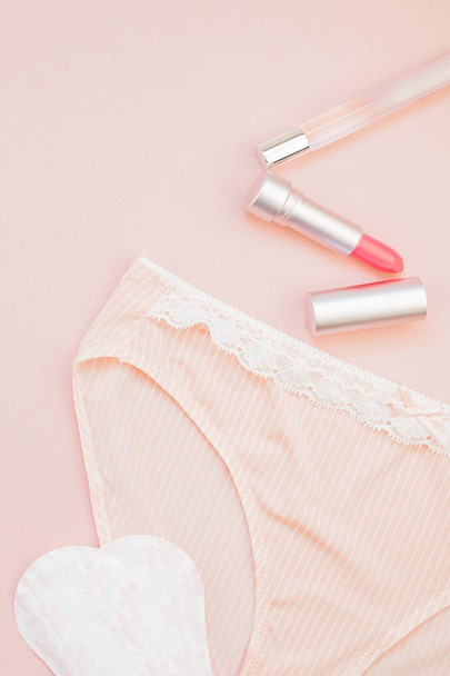 Feminine flat lay set of female panties and accessories, perfumes, lipstick and pads liners on pastel pink color background for fashion blog and social media with copy space for text - Photo, Image