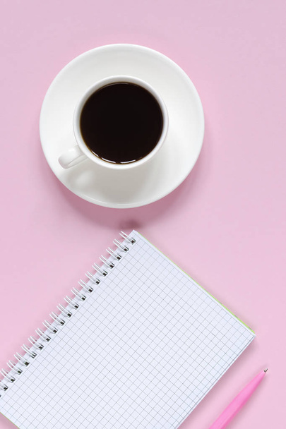 Open notebook with pink pen and coffee cup on pink background. Copy space background, top view flat lay overhead - Fotó, kép