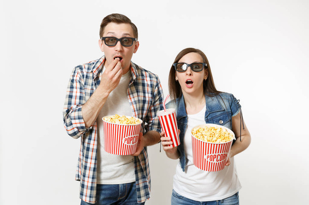 junges schockiertes Paar, Frau und Mann in 3D-Gläsern, die sich einen Film über Date ansehen, mit einem Eimer Popcorn, einem Plastikbecher Limo oder Cola isoliert auf weißem Hintergrund. Emotionen im Kinokonzept - Foto, Bild