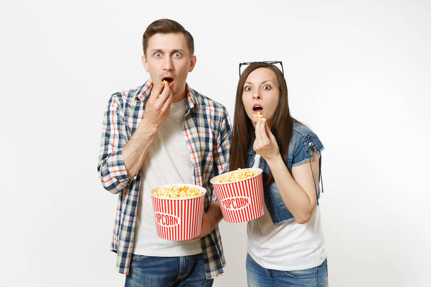 Молодые шокированные пара, женщина и мужчина в 3D-очках и повседневной одежде смотрят фильм на свидании, держа ведра попкорна, едят изолированные на белом фоне. Эмоции в концепции кино
 - Фото, изображение