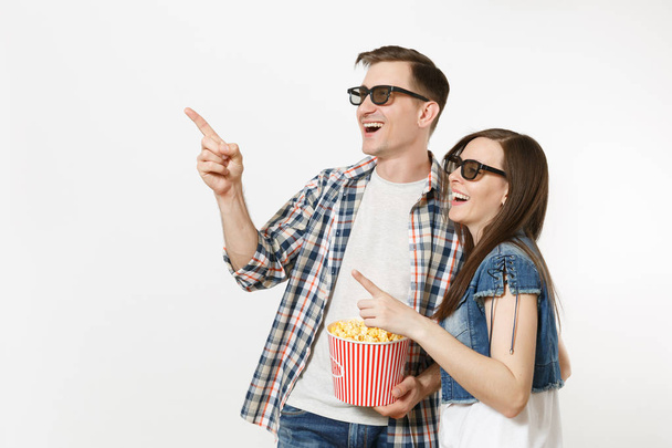 Mladý, usměvavý pár, Žena a muž v 3d brýlích sleduje film film na datum, držel kýbl popcornu, ukazující ukazováčků na copyspace izolovaných na bílém pozadí. Emoce v kině koncepce - Fotografie, Obrázek