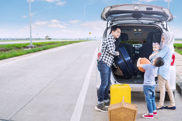 Image of young father with his family preparing suitcase into a car for a road trip. Shot on the roadside - Foto, Bild