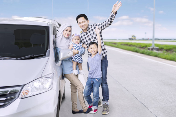 Portrait of Muslim family waving hands together at the camera while standing on the road near their car - Valokuva, kuva