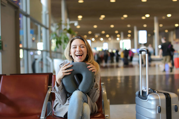 Жінка сидить з подушкою для шиї та багажем в залі очікування в аеропорту
. - Фото, зображення