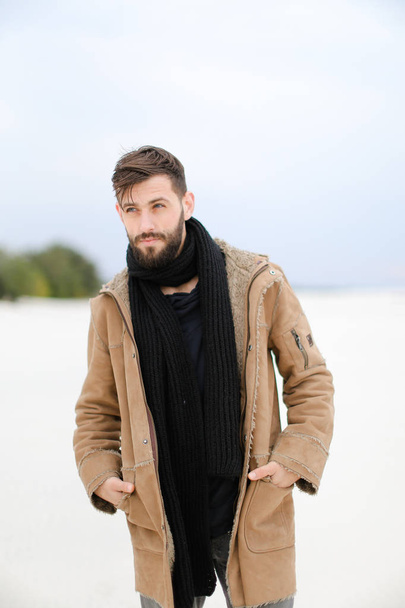 European male person with beard wearing coat and scarf standing in white snow background. - Photo, Image