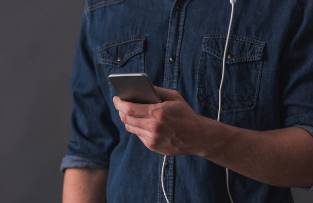 Обрізане зображення молодого чоловіка в навушниках використовує смартфон на сірому фоні
 - Фото, зображення