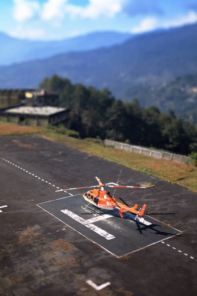 das Bild mit Hilfe einer Linse - der Hubschrauberlandeplatz mit dem orangefarbenen Helikopter auf ihr, vor dem Hintergrund des Himalaya - Foto, Bild