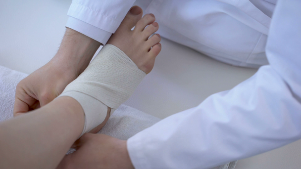 Lekarz bandażowanie skręconą kostkę, uruchomiona szkody po treningu nóg zbliżenie - Materiał filmowy, wideo