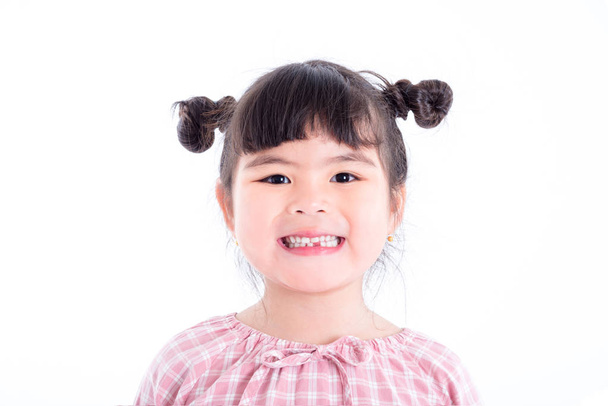 Μικρό ασιατικό κορίτσι να χαμογελάσει και να δείξει την πρώτη απώλειά του δόντια πάνω από λευκό - Φωτογραφία, εικόνα