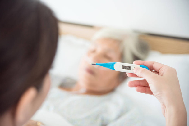 Krankenschwester hält Thermometer mit hohem Temperaturergebnis von Seniorin - Foto, Bild