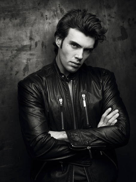 Black and white portrait of a man in a black leather jacket near wall - Фото, изображение