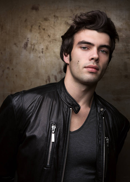 Young man in black leather jacket posing by metal walls. Portrait of the brunette in stylish clothes - Φωτογραφία, εικόνα
