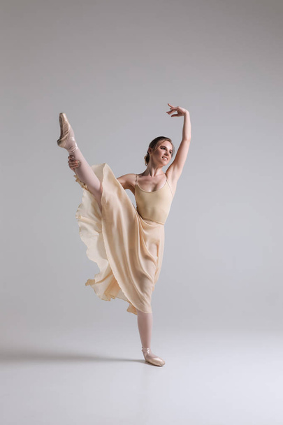 Making a dance! Graceful attractive charming young ballerina in beige outfit posing on toes on the studio background. - Foto, Imagen