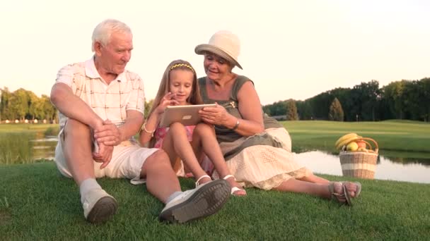 Пенсионеры и внучка используют планшет на открытом воздухе
. - Кадры, видео
