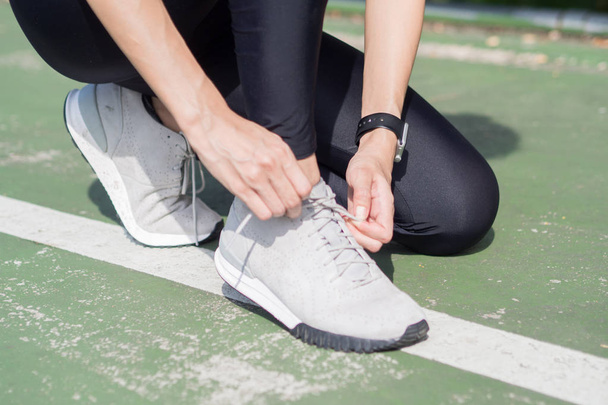 Close up of young woman lace up her shoe ready to workout on exercising in the park with warm light sunshine in morning. Young woman prepare for outdoor exercise in park. Outdoor exercise concept. - Foto, Imagen