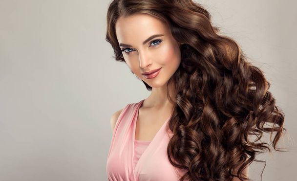 Brunette girl with long , healthy and shiny curly hair . Beautiful model woman with wavy hairstyle .Care and beauty - Fotografie, Obrázek
